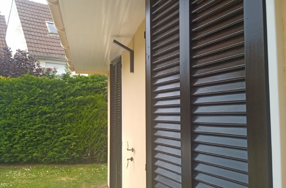 Volets en bois lasurés foncé sous un avant-toit